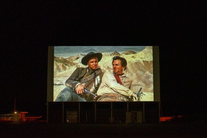 An old western movie projected onto the drive-in movie screen at night.
