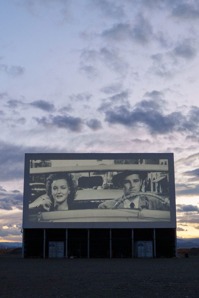 Drive-in movie screen showing an old black and white movie.