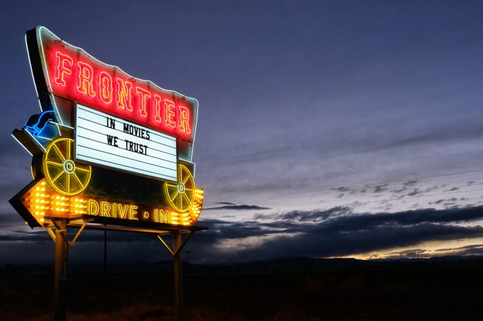 Neon Frontier Drive-Inn sign that says IN MOVIES WE TRUST.