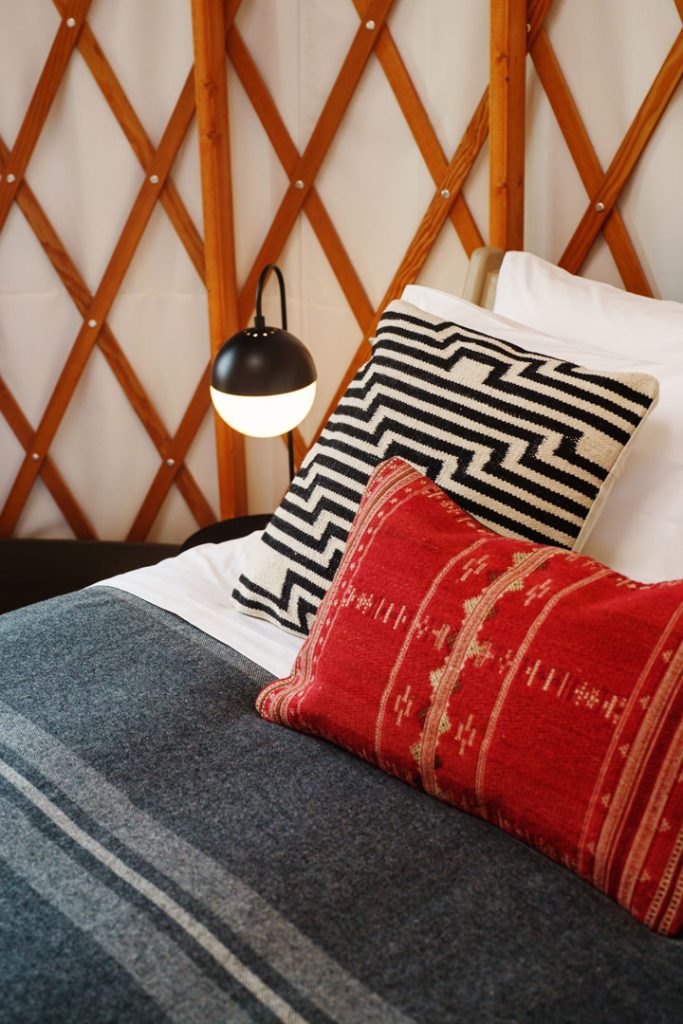 Close up view of a black and white pillow and a red pillow on a bed with a charcoal gray blanket in a yurt