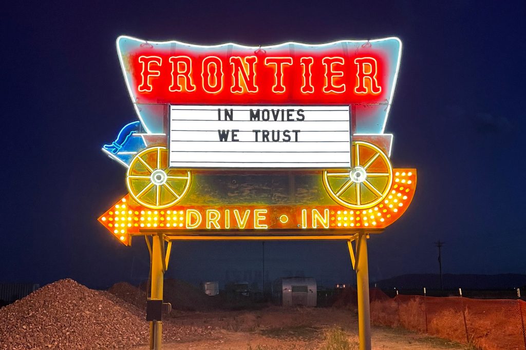 Neon Frontier Drive-Inn sign that says IN MOVIES WE TRUST.