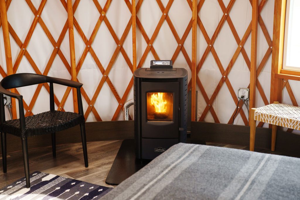 Close up of a burning pellet stove in a yurt with a chair and bench on either side