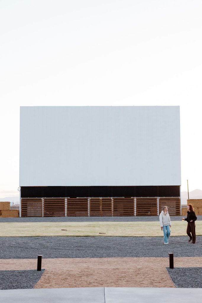 The movie screen at the Frontier Drive Inn before dark with two people walking nearby